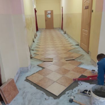 Mężczyzna kładzie płytki w holu szkoły.