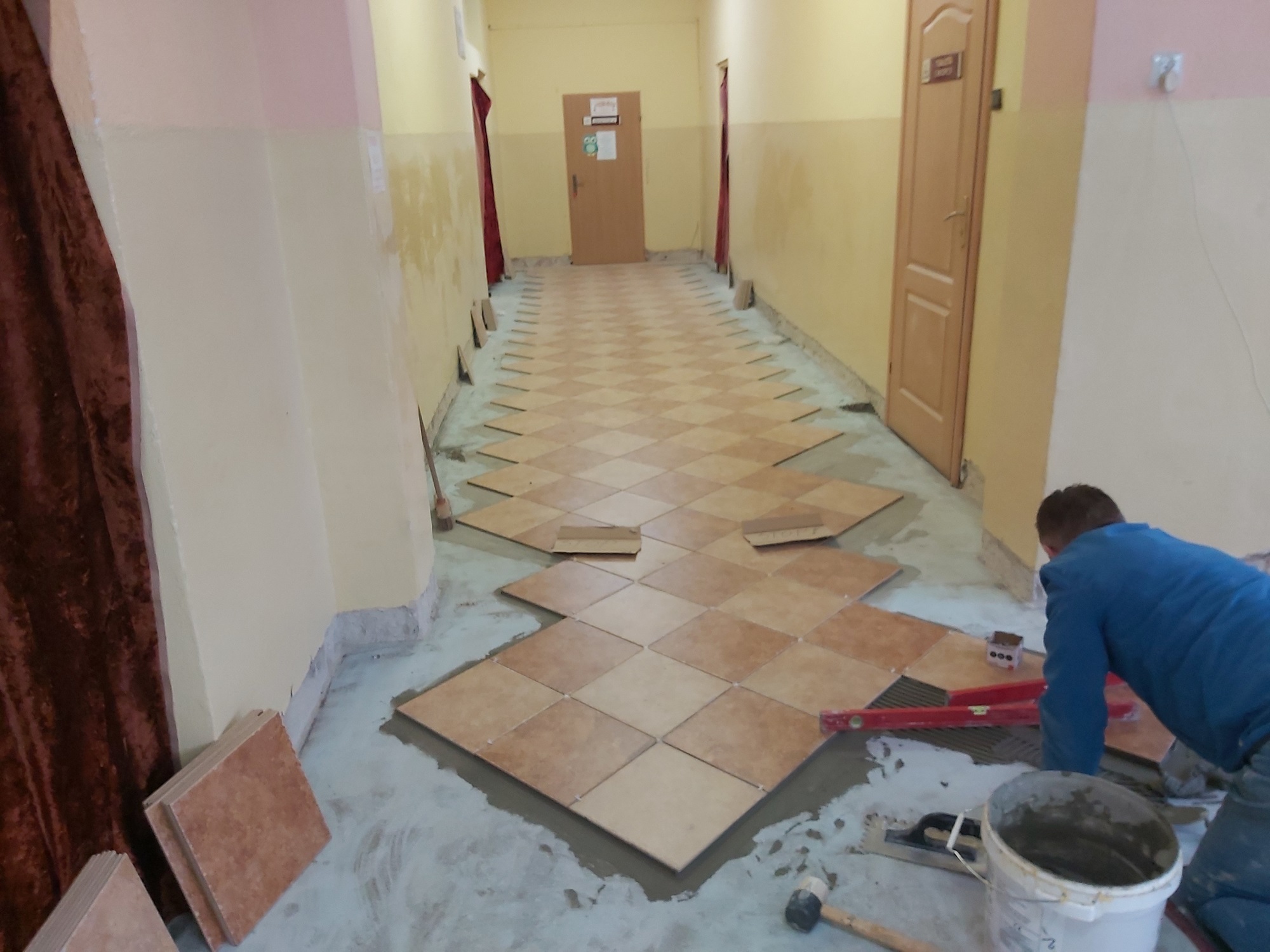 Mężczyzna kładzie płytki w holu szkoły.