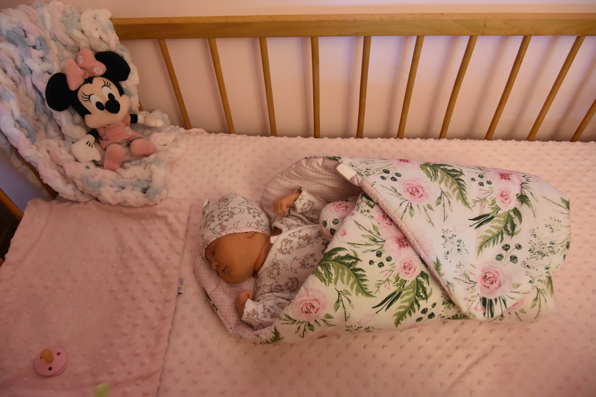 Śpiąca malutka dziewczynka zawinięta w rożek leżąca w łóżeczku drewnianym.