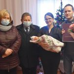 Cztery osoby, w tym kobieta w średnim wieku i straszy mężczyzna oraz młoda kobieta i mężczyzna pozują do pamiątkowego zdjęcia. Młoda kobieta trzyma na rękach dziecko, zaś mężczyzna kwiaty.