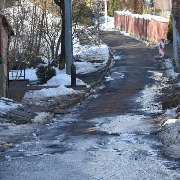 Droga asfaltowa bardzo zniszczona, koleiny, dziury. Prowadzi między budynkami wielorodzinnymi.
