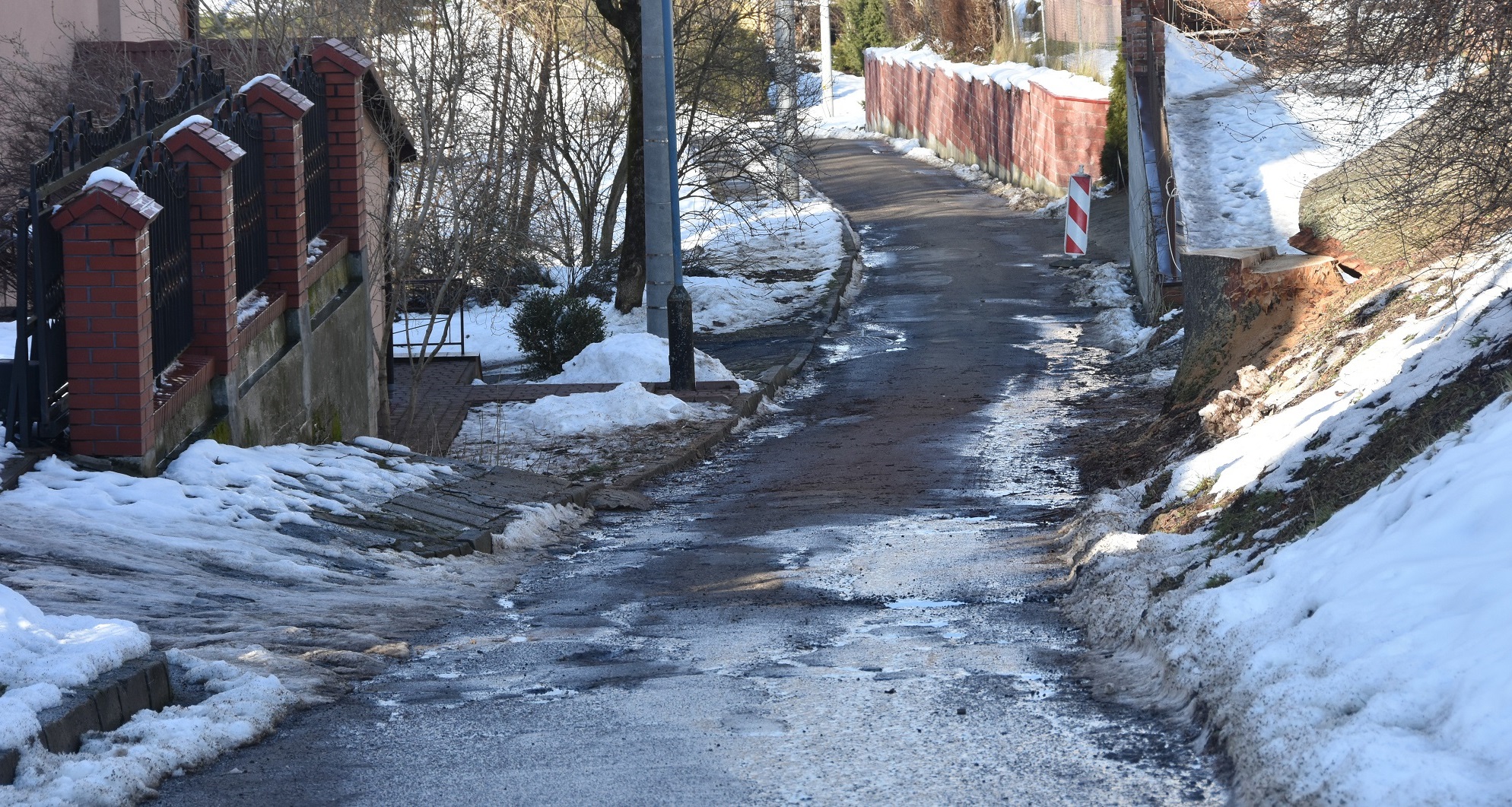 Droga asfaltowa bardzo zniszczona, koleiny, dziury. Prowadzi między budynkami wielorodzinnymi.