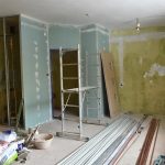 Pomieszczenie w remoncie. Wewnątrz obdarte ściany, Na środku stoi stelaż, na podłodze leżą narzędzia do robót wykończeniowych.