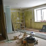 Pomieszczenie w remoncie. Wewnątrz obdarte ściany, Na środku stoi stelaż, na podłodze leżą narzędzia do robót wykończeniowych.