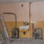 Obdarte mieszkanie. Na wprost znajduje się stary piec, umywalka.