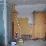 Obdarte ściany w mieszkaniu gminnym. Z boku są drzwi, zas z drugiej strony postawione są działki działowe na łazienkę.