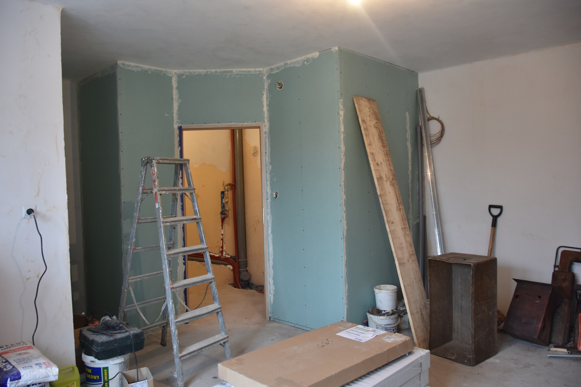 Pomieszczenie wewnątrz budynku. Trwają w nim prace remontowe. Są brudne ściany, podłoga nie ma paneli, postawione są ścianki, z których powstanie łazienka.