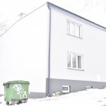 Budynek z nową szarą elewacją w scenerii zimowej. Przed budynkiem stoi kontener zielony.