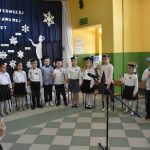 Grupa dzieci stoi w półkolu z podniesionymi prawymi rękami i składa ślubowanie na ucznia szkoły.