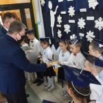 Dwóch mężczyzn przekazuje grupie dzieci drobne upominki - w postaci kredek, długopisów, flamastrów.