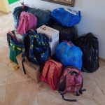 Zapakowane plecaki w różnych kolorach i niebieski oraz czarne worki. Znajdują się one w jasnym pomieszczeniu.