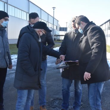 Pięciu mężczyzn w ciemnych ubraniach stoją na ulicy i rozmawiają.