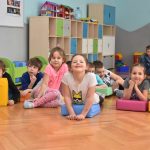 Grupa dzieci w sali zajęć. Kilka z nich leży na siedziskach.