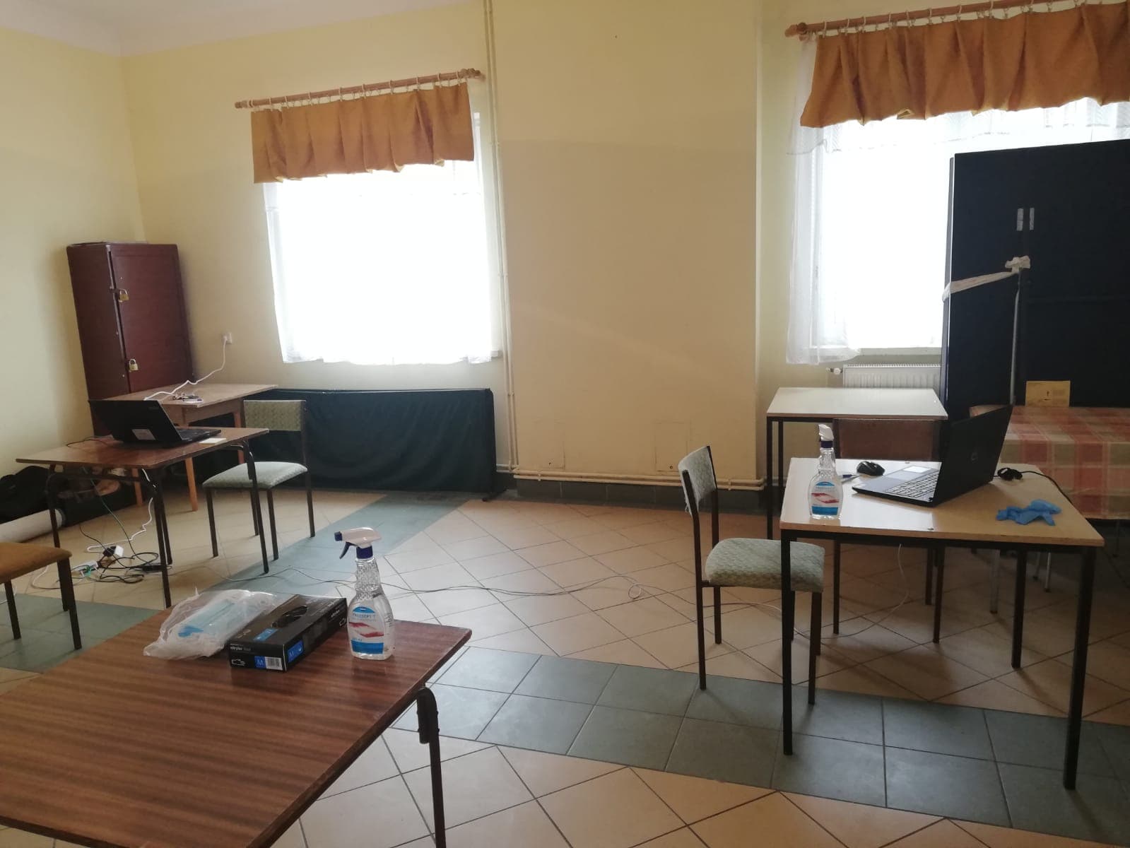 Jasne pomieszczenie w budynku. Stoją w nim stoliki, na których leżą laptopy.