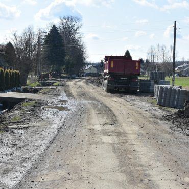 Droga w trakcie przebudowy. Po lewej stronie zabudowa mieszkaniowa, po prawej stronie stoi duża ciężarówka.