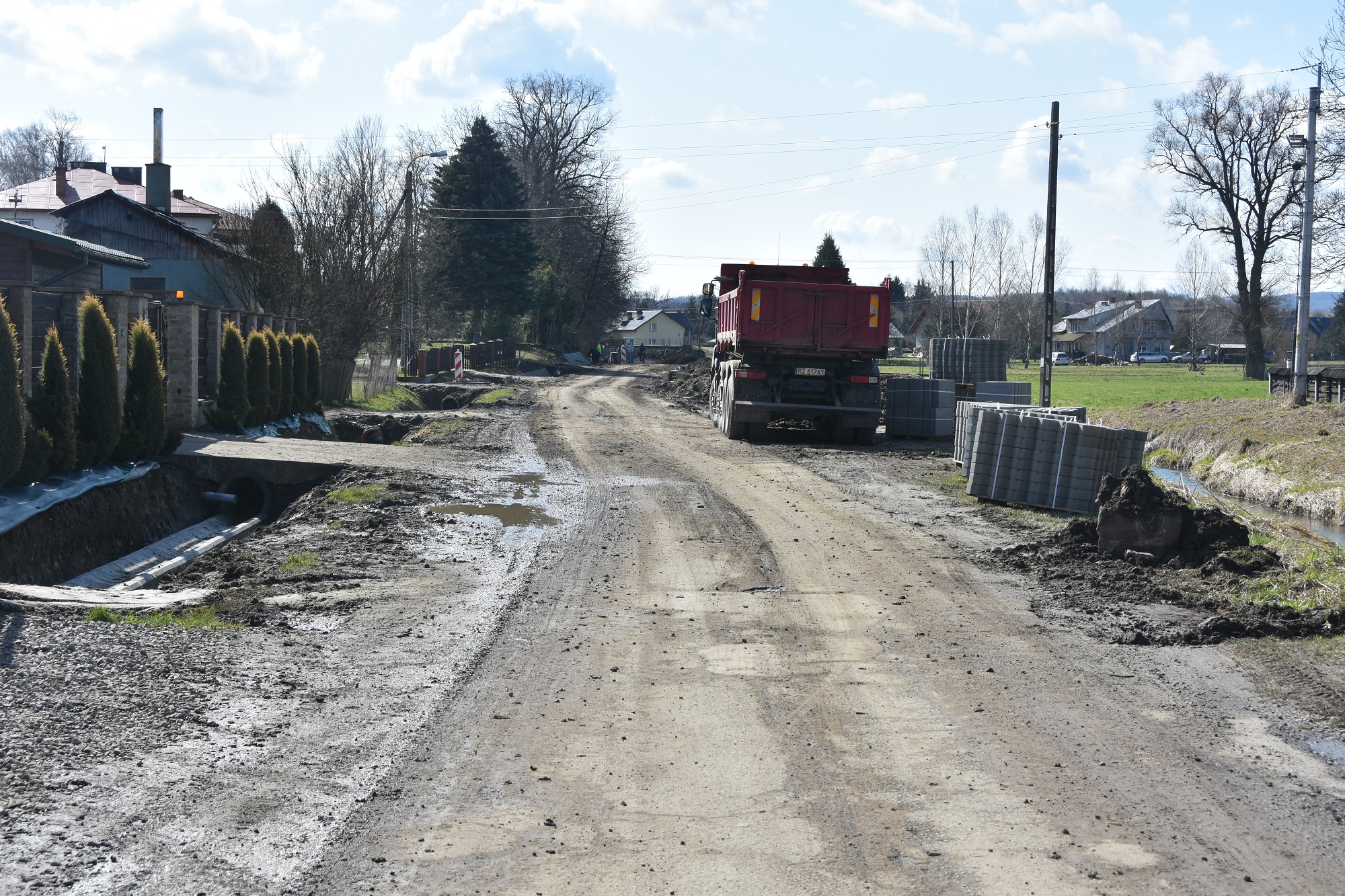 Droga w trakcie przebudowy. Po lewej stronie zabudowa mieszkaniowa, po prawej stronie stoi duża ciężarówka.