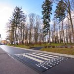 Nowo wyremontowana droga asfaltowa, na ulicy zrobiony przy szkole próg zwalanijący, po prawej stronie park.