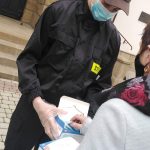 Młody chłopak w stroju strażaka w maseczce rozdaje maseczki kobiecie.