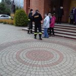 Dwóch mężczyzn w stroju strażaka z napisem na plecach straż pożarna rozdaje maseczki ludzi.