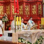 Trzech księży odprawia msze św. Za nimi stoją ministranci w czerwonych sutannach.