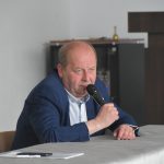 Starszy mężczyzna siedzi przy stoliku i przemawia do mikrofonu.