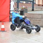 Chłopiec w niebieskiej kurtce jeździ gokartem między czerwonymi pachołkami na płycie Rynku.