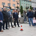 Grupa mężczyzn stoi na Rynku i rozmawia. Za nimi ustawiony namiot. Obok Ludzie stoją z dziećmi.