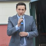 Młody mężczyzna w garniturze przemawia na rynku do mikrofonu.