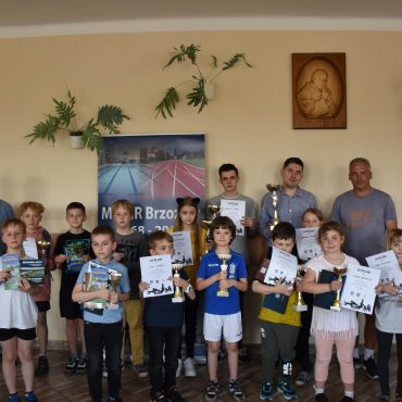 Grupa kilkudziesięciu dzieci trzyma puchary i dyplomy w rękach. Obok nich stoi trzech mężczyzn