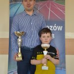 Dwie osoby, mężczyzna i chłopiec trzymają w rękach puchary, na tle baneru MOSIRU.