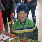 Mały chłopczyk w zielonej kurtce stoi przy stoliku, na którym leżą warzywa oraz ludzik z nich zrobiony.