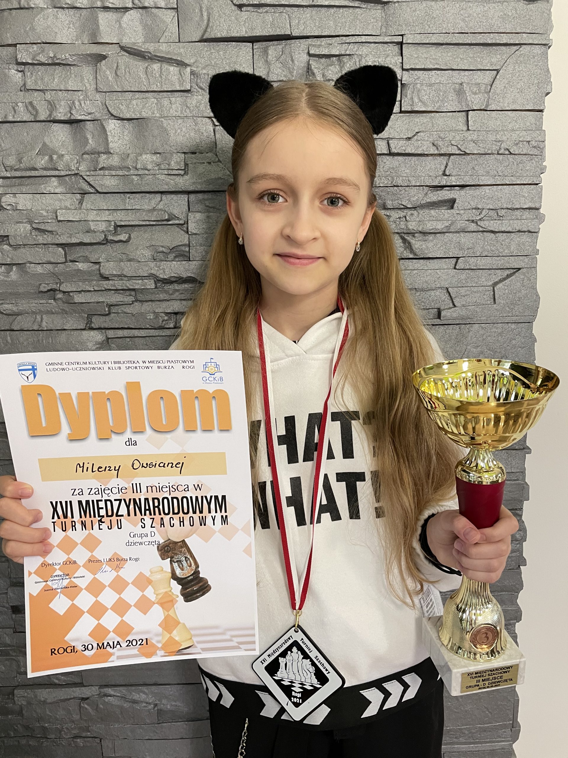 Dziewczynka o jasnych włosach trzyma w rękach puchar i dyplom.