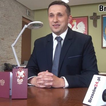 Młody mężczyzna w garniturze siedzi przy stoliku, przed nim leży legitymacja i odznaczenie.