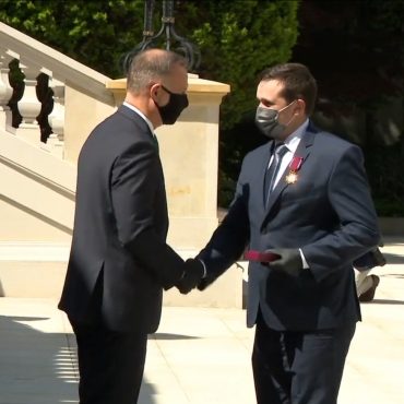 Dwóch mężczyzn w garniturach podaje sobie dłonie na placu.