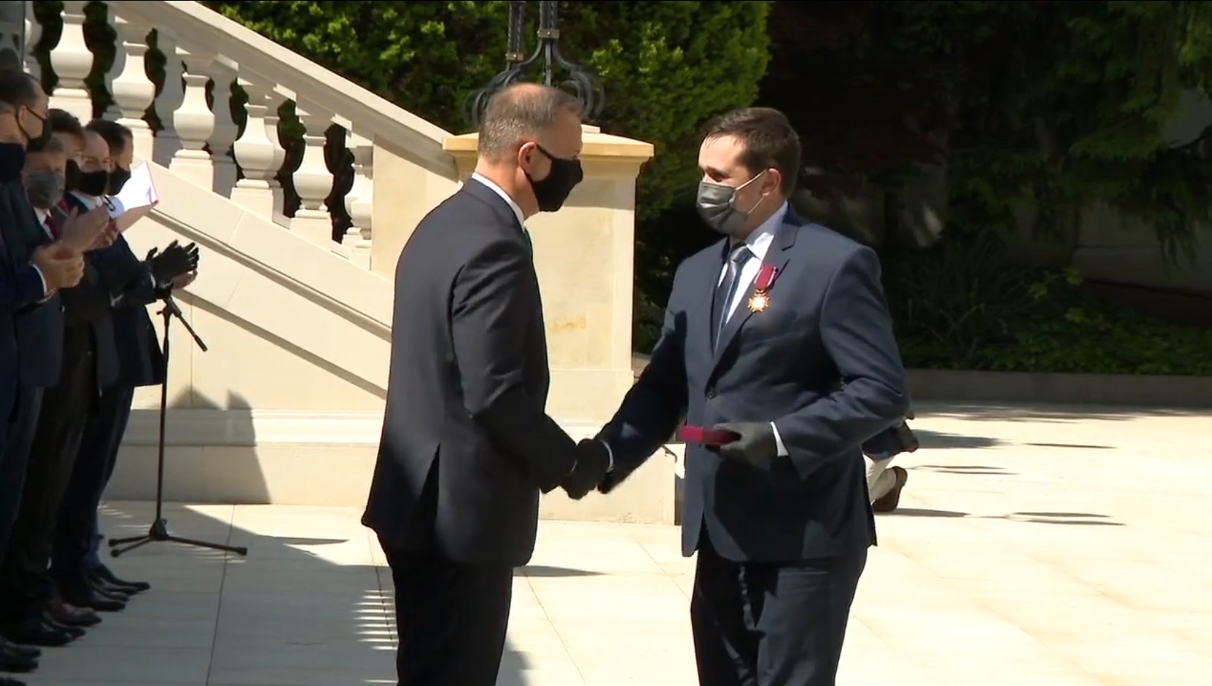 Dwóch mężczyzn w garniturach podaje sobie dłonie na placu.