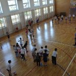 Dzieci w strojach sportowych ćwiczą na sali gimnastycznej.