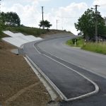 Chodnik wzdłuż drogi powiatowej po prawej stronie, po lewej stronie tereny zielone.