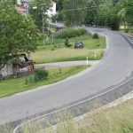 Nowy chodnik wzdłuż drogi powiatowej po prawej stronie. Po lewej stronie tereny zielone z zabudowaniami mieszkalnymi.