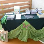 Zestaw nagród książkowych wyłozonych ksiązkamii nagrodami. Stolik wyłożony zielonym obrusem.