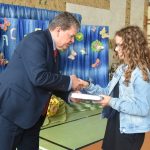 Mężczyzna w garniturze przekazuje na ręće dziewczynce w katanie jeansowej książkę.