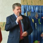 Mężczyzna w garniturze grantowym przemawia do mikfronu na sali gimnastycznej.