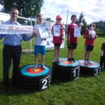 Grupa dzieci ze starszym mężczyzną pozują na podium, z dyplomami.