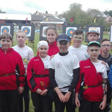 Grupa dzieci stoi na zewnątrz. Część z nich ubrana na biało, część na czerwono.