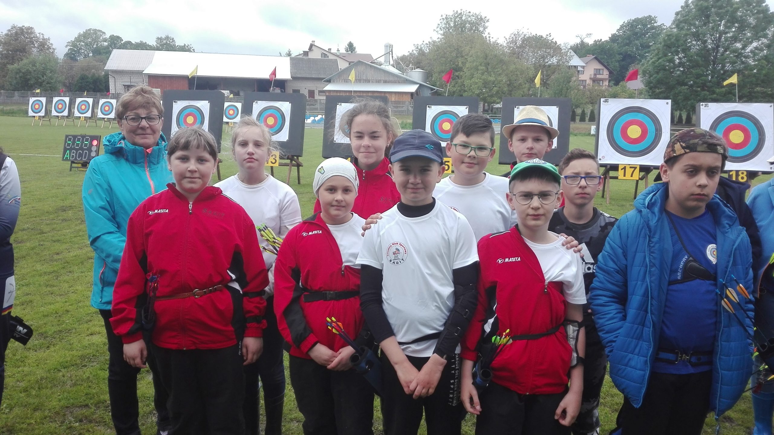 Grupa dzieci stoi na zewnątrz. Część z nich ubrana na biało, część na czerwono.