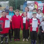 Dzieci ubrane w czerwony swetry stoją z dyplomami.