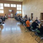 Dzieci siedzą przy stolikach i grają w szachy na sali gimnastycznej.