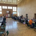 Dzeci i młodzież siedzą przy stolikach i grają w szachy na sali gimnastycznej.