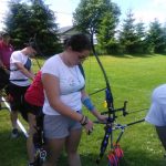 Grupa dzieci ubrana na sportowo przygotowuje się do strzału z łuku.