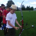 Grupa dzieci - chłopców ubrana na sportowo przygotowuje się do strzału z łuku.