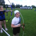 Dziewczynka ubrana na sportowo przygotowuje się do strzału z łuku na zewnątrz.